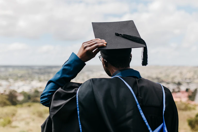 Rear view of male in academic gown, hood and cap, looking out over a distant landscape
