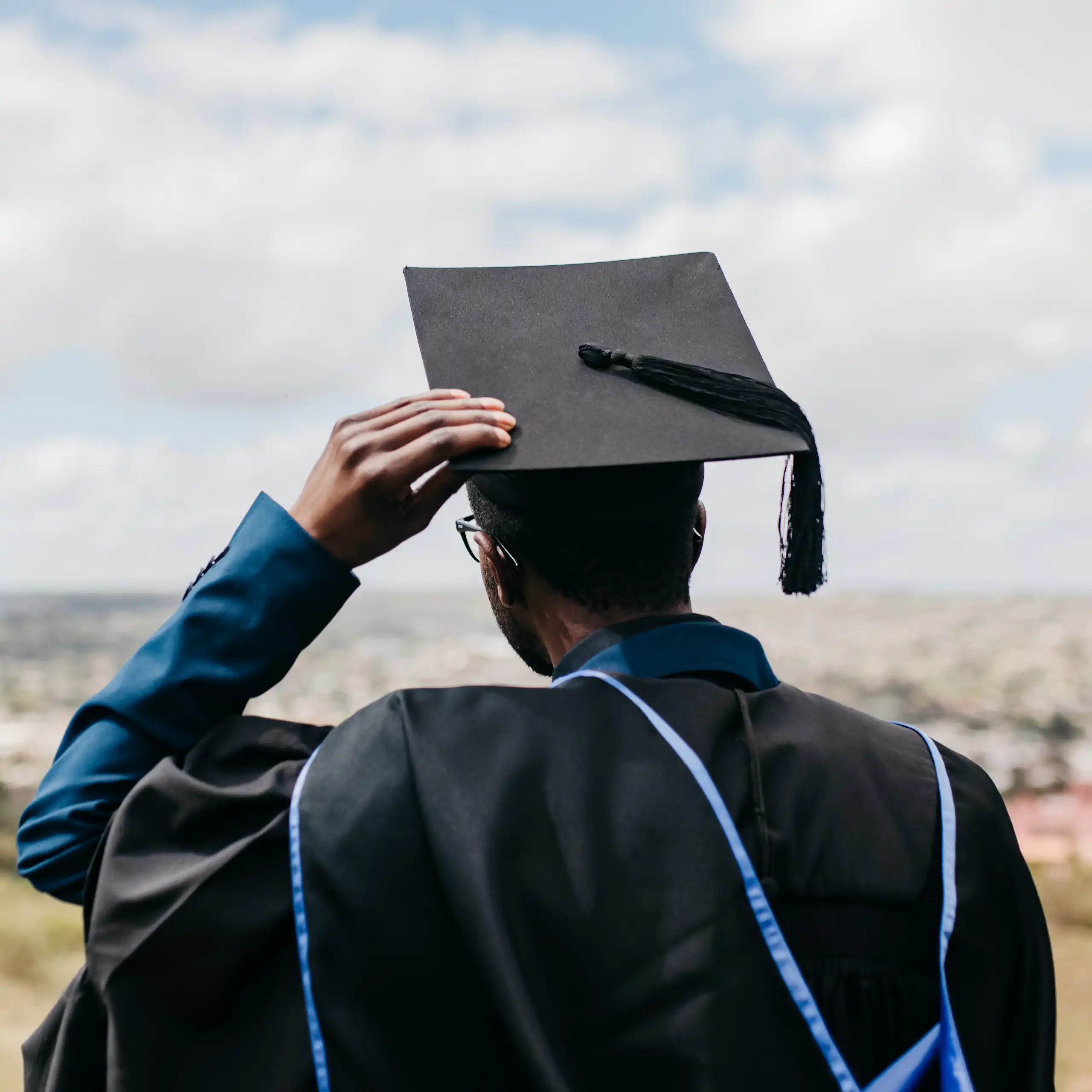 Rear view of male in academic gown, hood and cap, looking out over a distant landscape