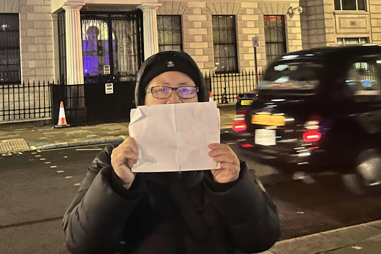 A woman olds upo a blank sheet of paper in front of her face on a London street.
