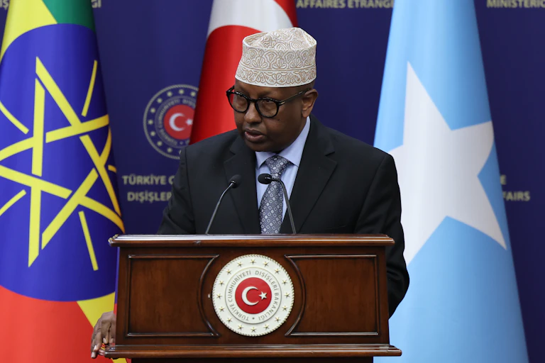 A man speaking into a microphone with three flags behind him