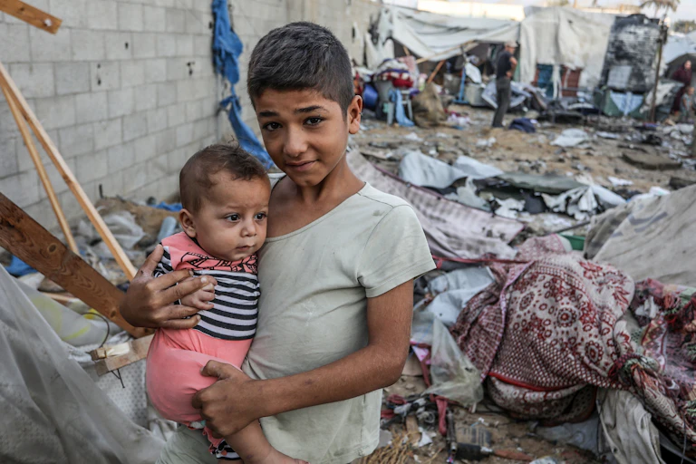 Un jeune garçon tient une enfant dans ses bras parmi les décombres.