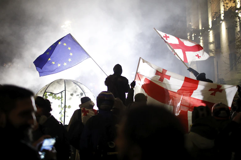 Street protests in Tbilisi, Georgia with people carrying EU and Georgian flags.