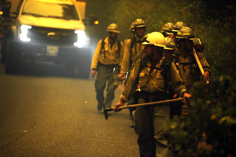 A crew from Idaho carries equipment as they walk down a smoky road while working a fire in the Shasta-Trinity National Forest in California in 2021.