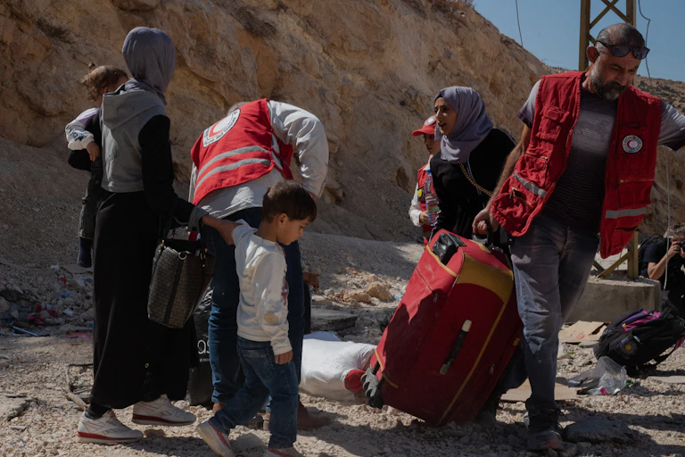 A group of men and women lift luggage on a dirt road.