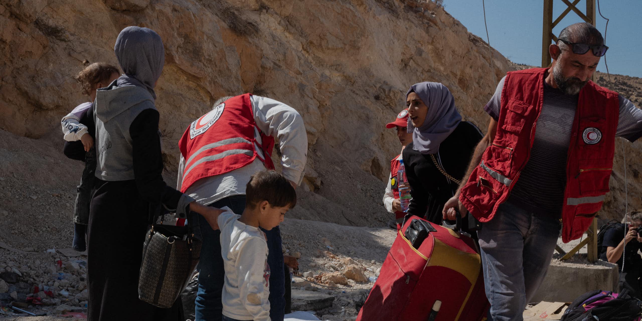 A group of men and women lift luggage on a dirt road.