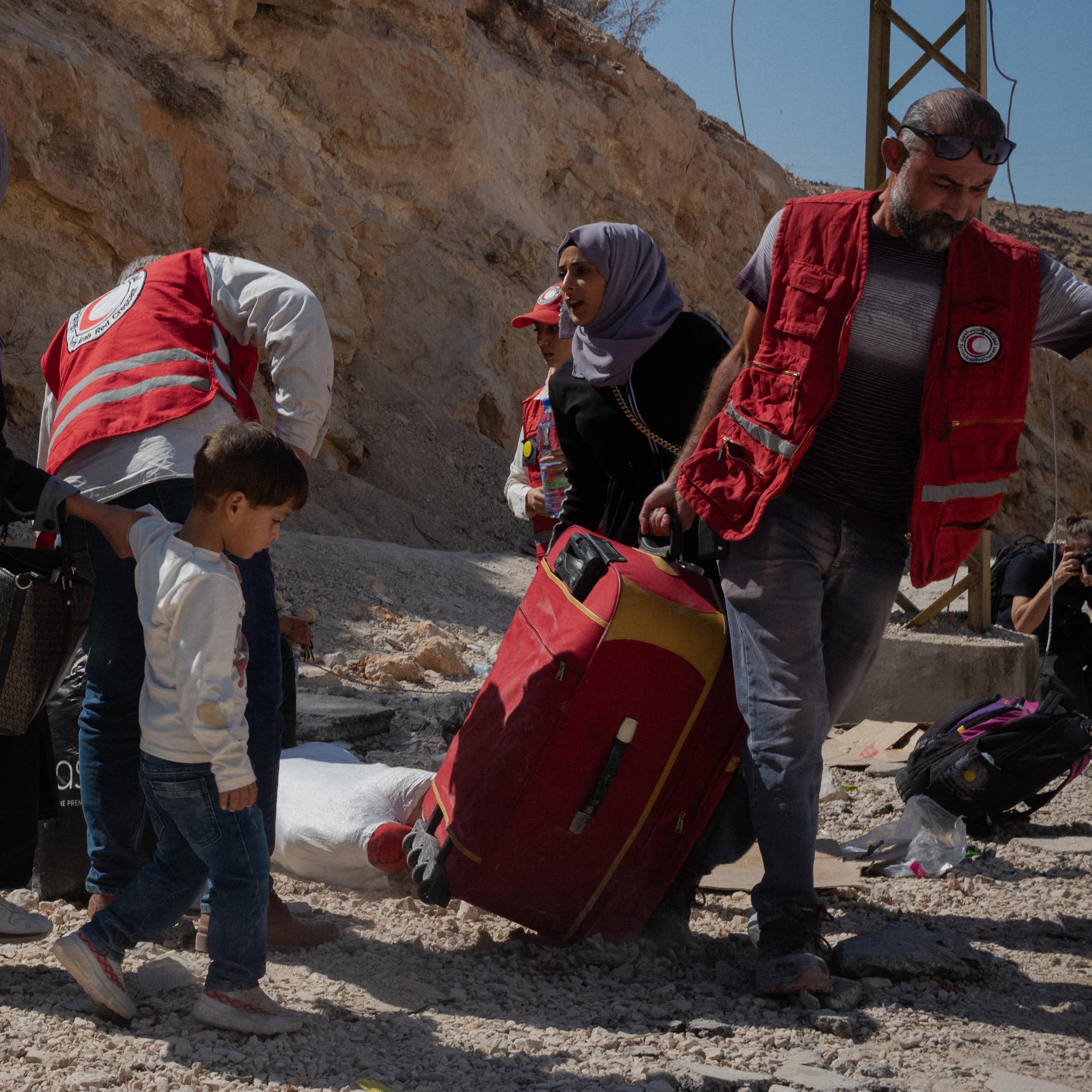 A group of men and women lift luggage on a dirt road.