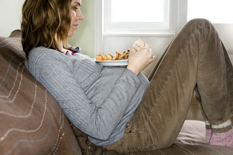 Pregnant woman sitting on couch with a plate of healthy food on her pregnant belly.
