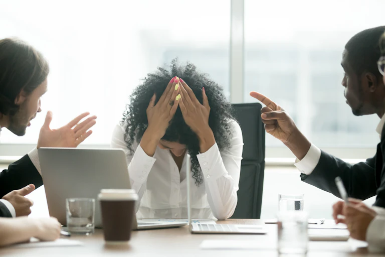 A stressed female professional puts her head in her hands as two leaders berate her.
