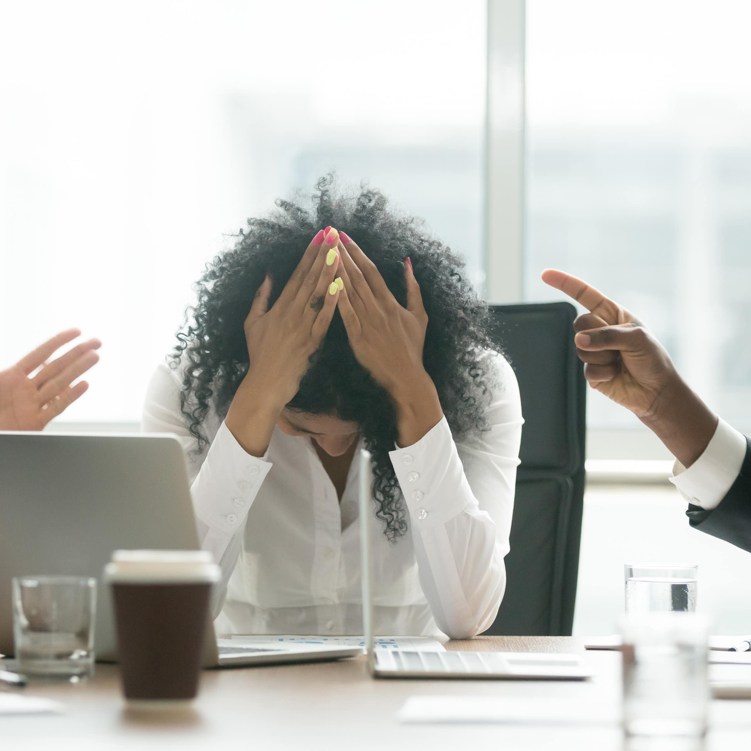 A stressed female professional puts her head in her hands as two leaders berate her.