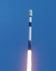 Against a blue sky, a rocket shoots off into space.