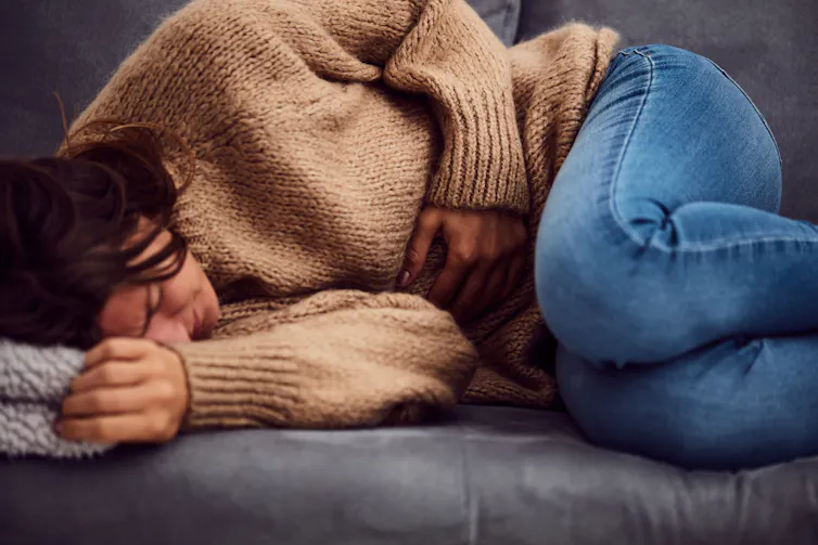 A woman curled up on a couch, holding her stomach and grimacing in pain