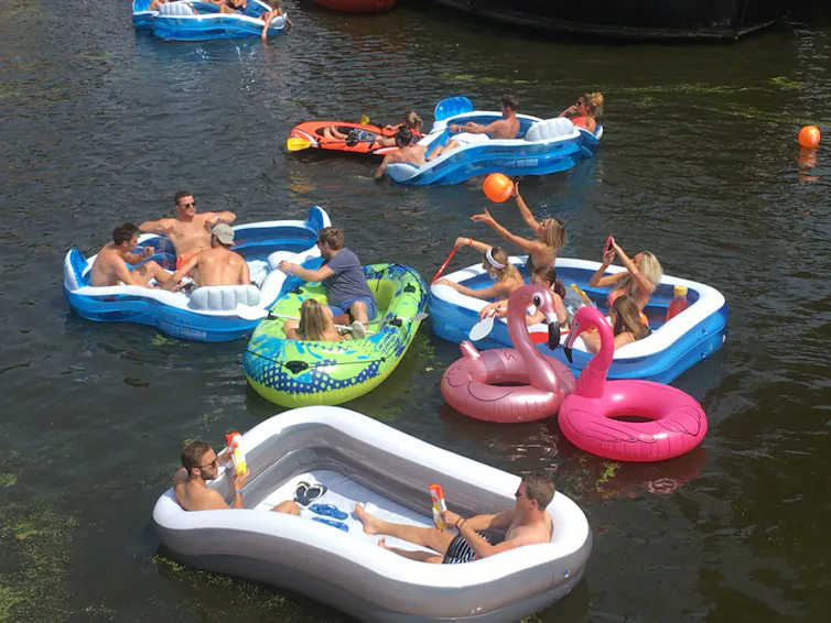 Young adults in inflatable boats, lilos on river, relaxing