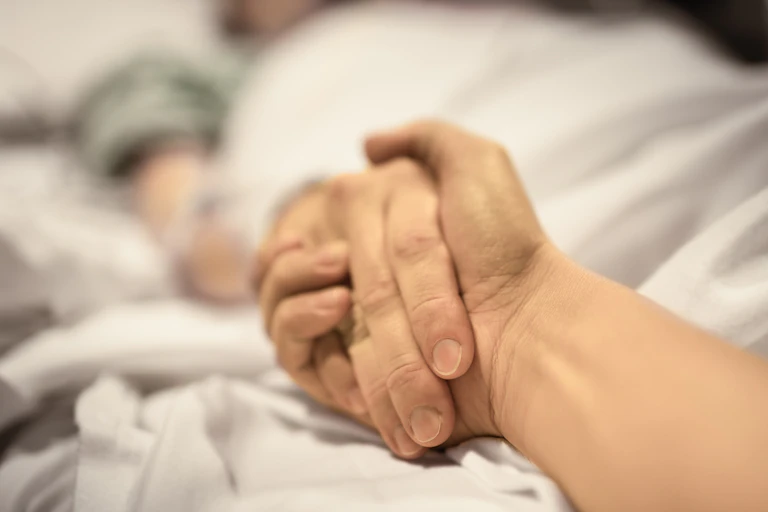 Hand clasps another hand of someone lying in a hospital bed