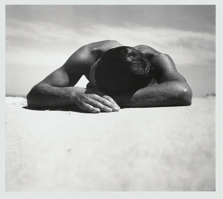 A suntanned man lying on a beach.