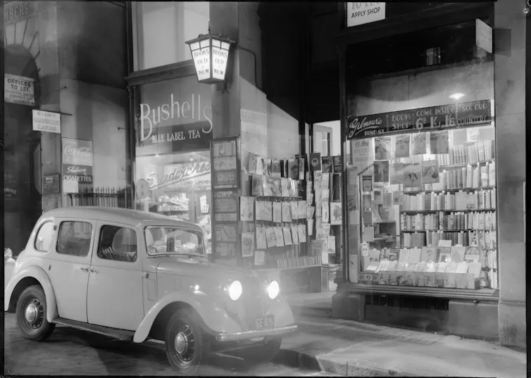 A black and white photo of a car in front of a bookshop.