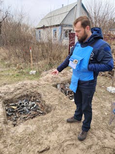 A man points to a pit filled with bits of destroyed weapons.