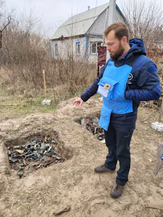Un homme montre du doigt une fosse remplie de morceaux d’armes détruites.