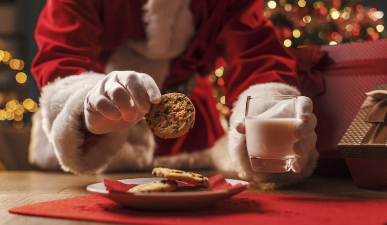 hands of man in red and white santa costume reach for cookies and milk