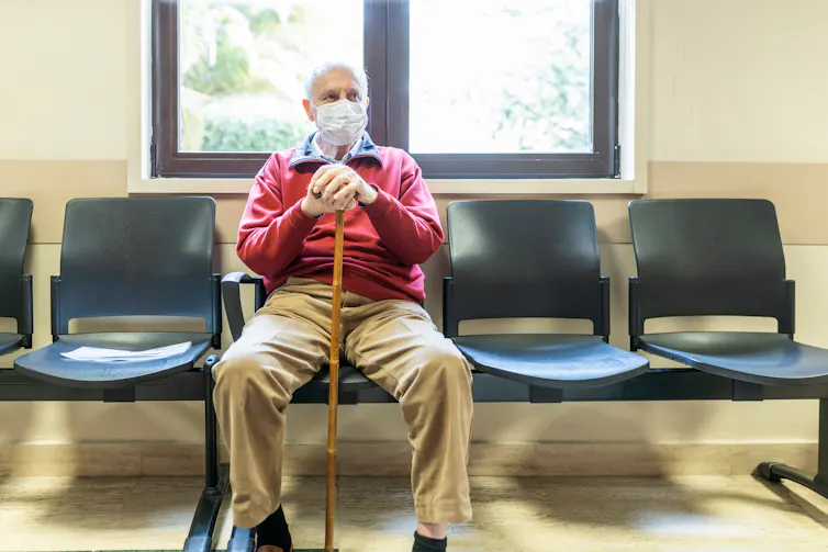 An elderly man with a mask waits in a doctor's office.
