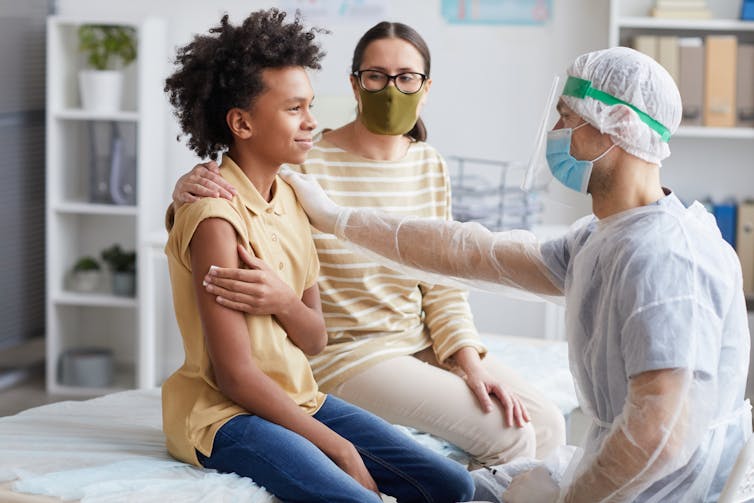 A teenage boy in a clinic holding his upper arm after a vaccination.