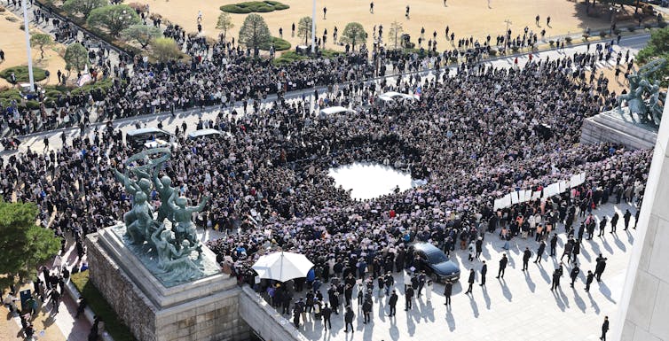 A large crowd of protesters in a public square in front of a line of security guards.