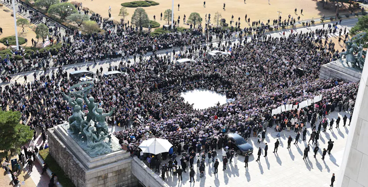 A large crowd of protesters in a public square in front of a line of security guards.