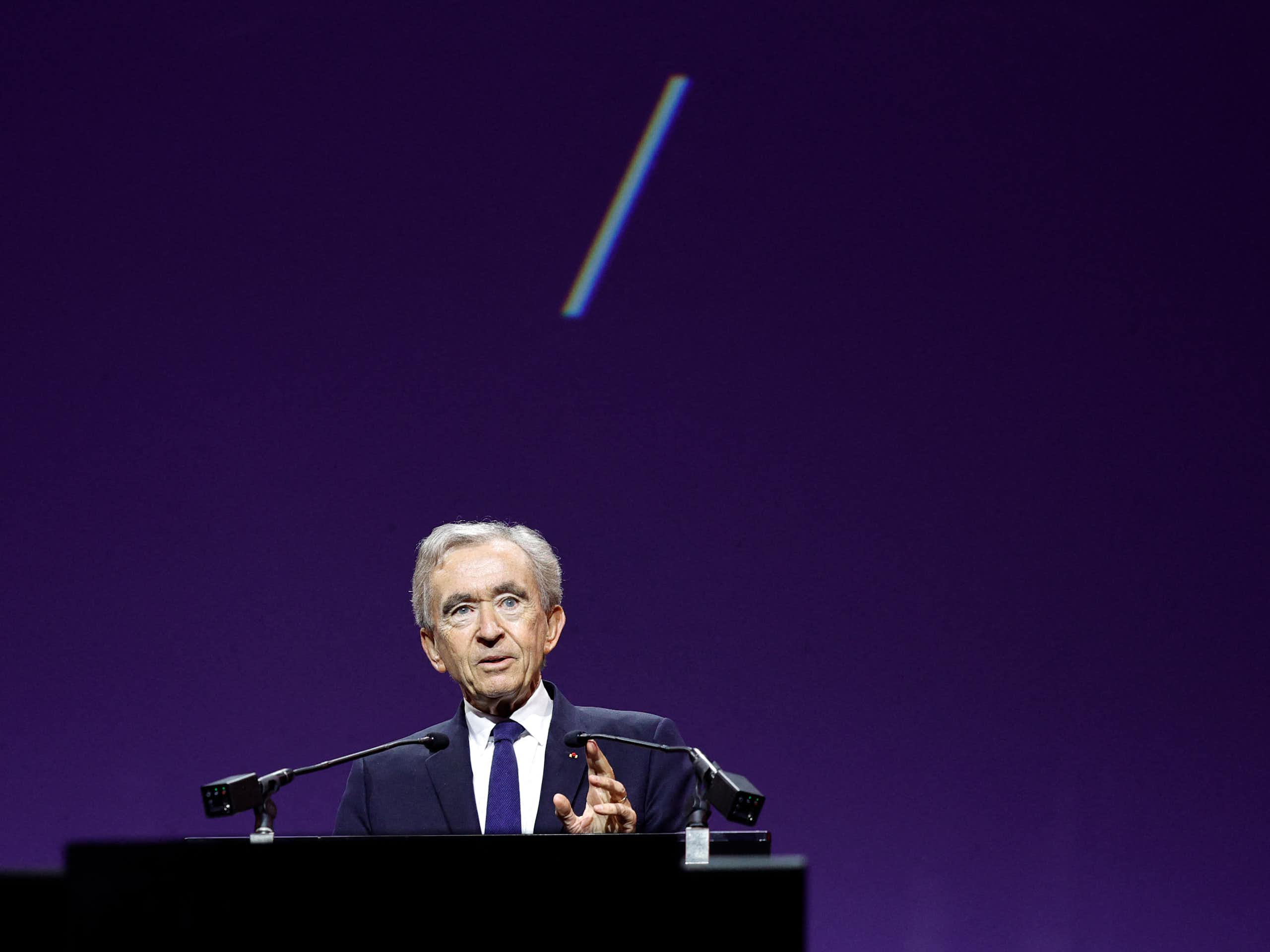 Bernard Arnault speaks at a lectern in front of a purple background.