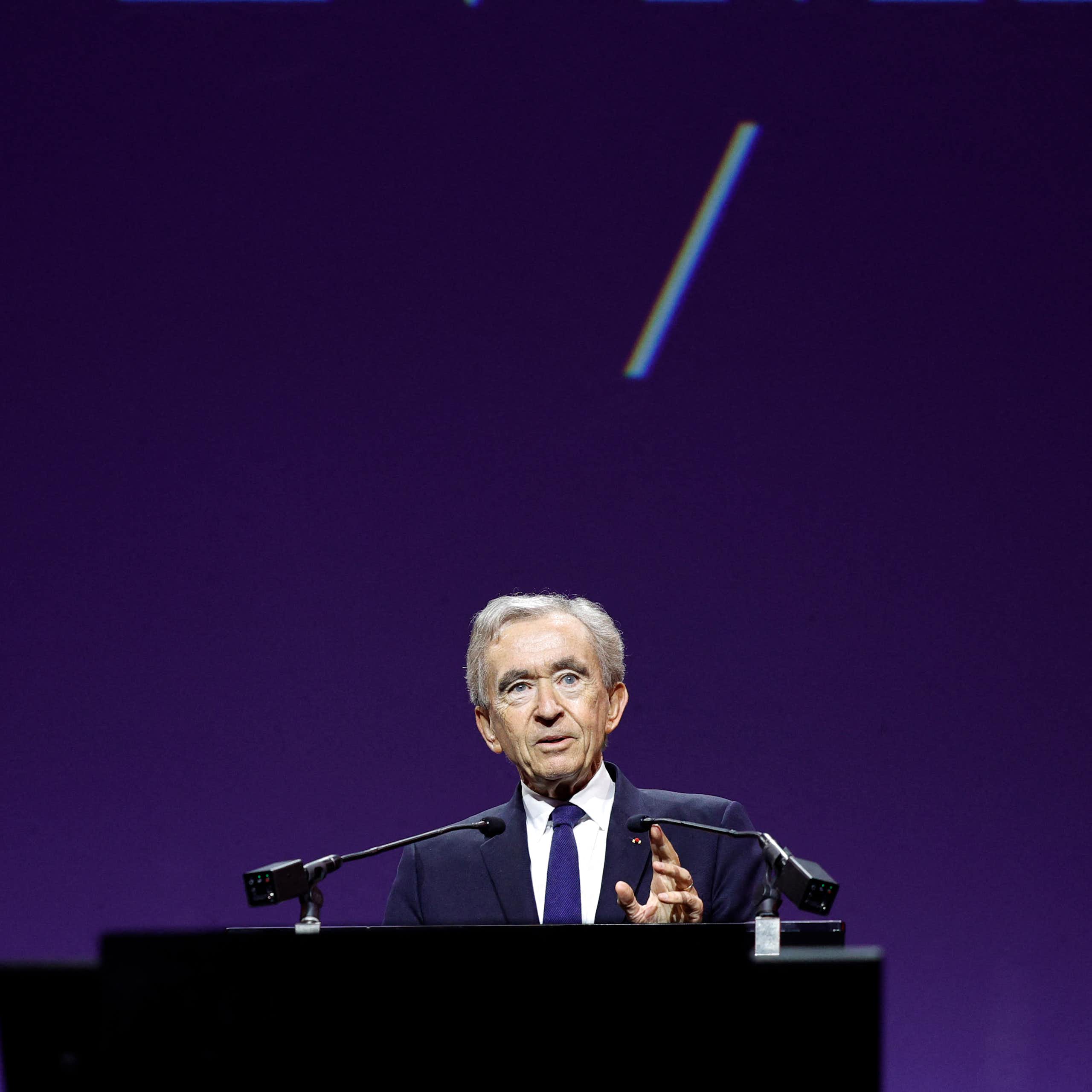 Bernard Arnault speaks at a lectern in front of a purple background.