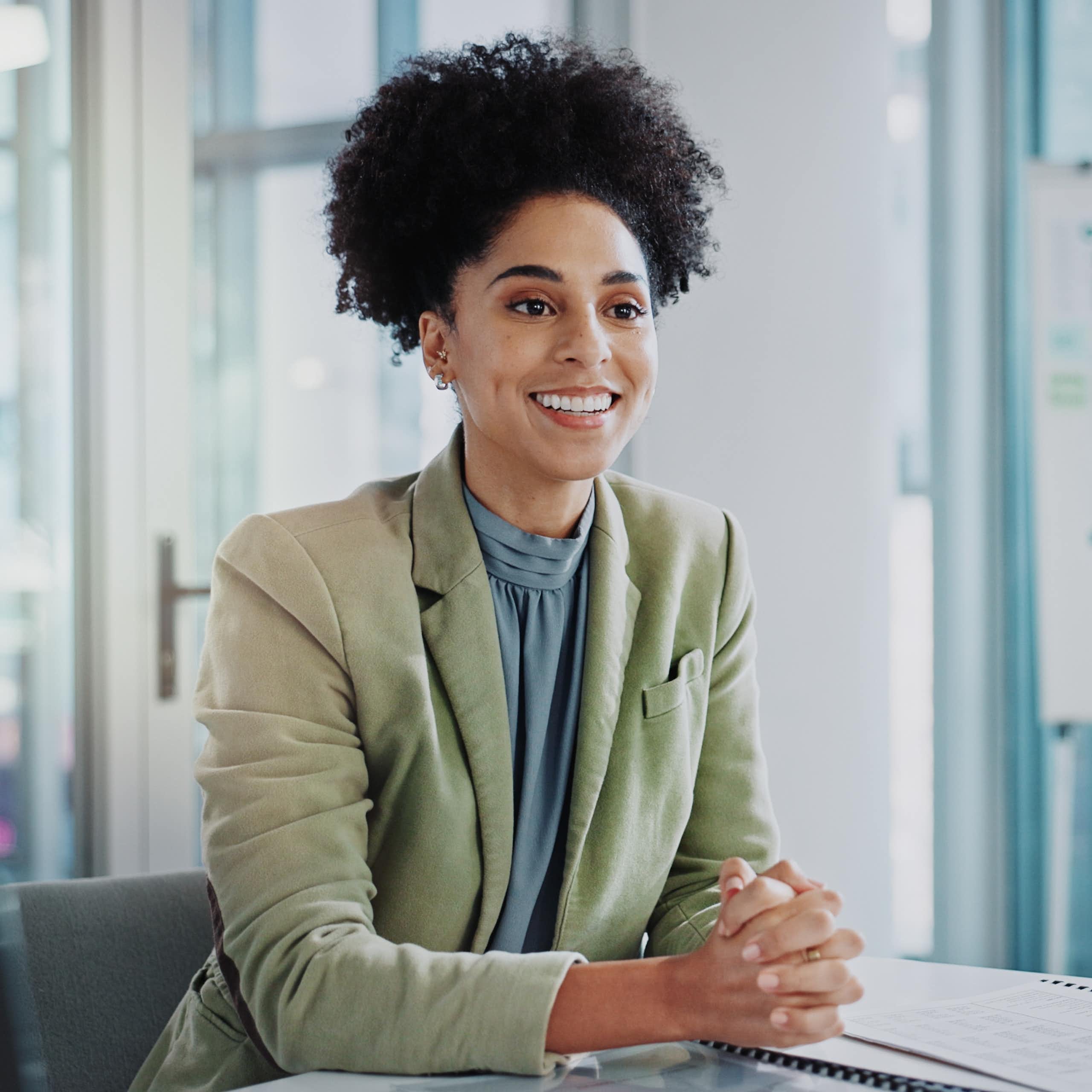 A woman sitting in an office smiles at the person sitting across from her.