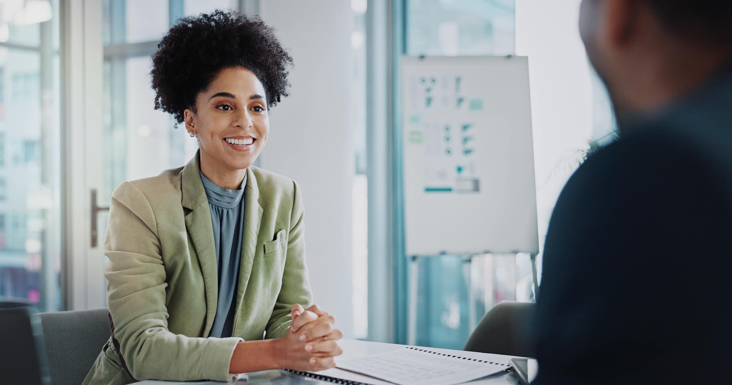 A woman sitting in an office smiles at the person sitting across from her.