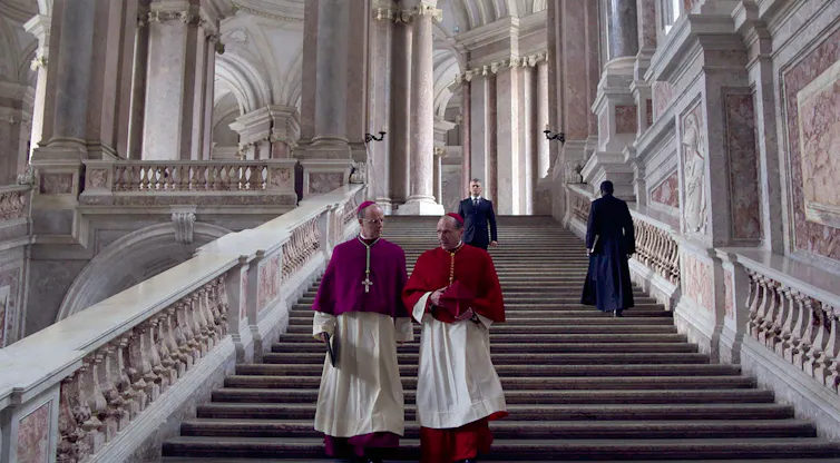 Two cardinals walking down a grand marble staircase in the Vatican.
