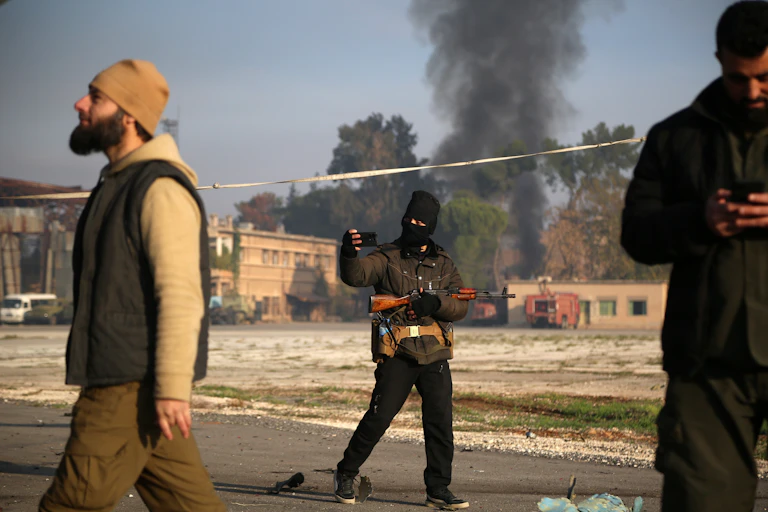 An armed man takes a selfie as billows of smoke pour out of a burning building.