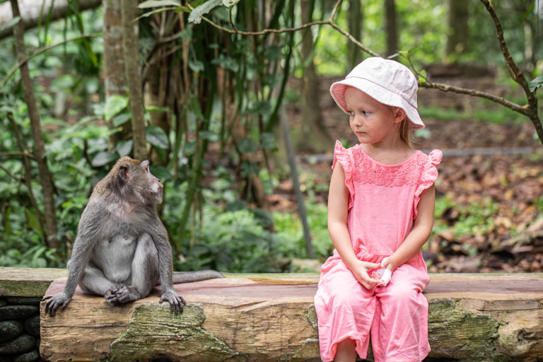 Monkey and girl sitting next to each other and looking at each other