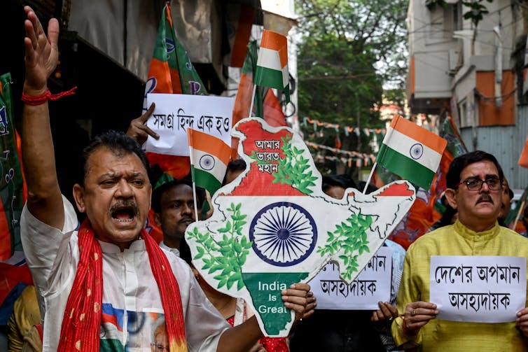 Men march down the street holding replica maps of India with the Indian flag on them.
