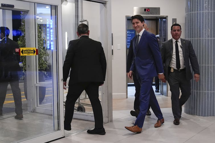 A man in a dark suit and brown leather shoes smiles as he walks through a hotel lobby.