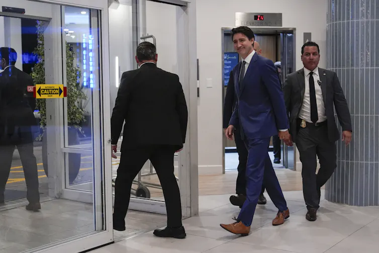 A man in a dark suit and brown leather shoes smiles as he walks through a hotel lobby.