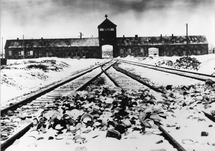 A black-and-white photo shows rail tracks leading to an infamous concentration camp.