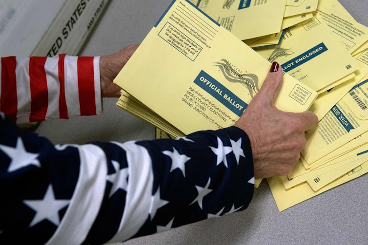 Election worker in jacket with US flag sorts official ballots for Colorado.