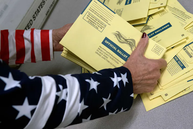 Election worker in U.S. flag jacket sorts official Colorado election ballots.