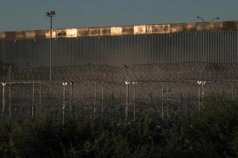 A large metal wall is seen in front of barbed wire.
