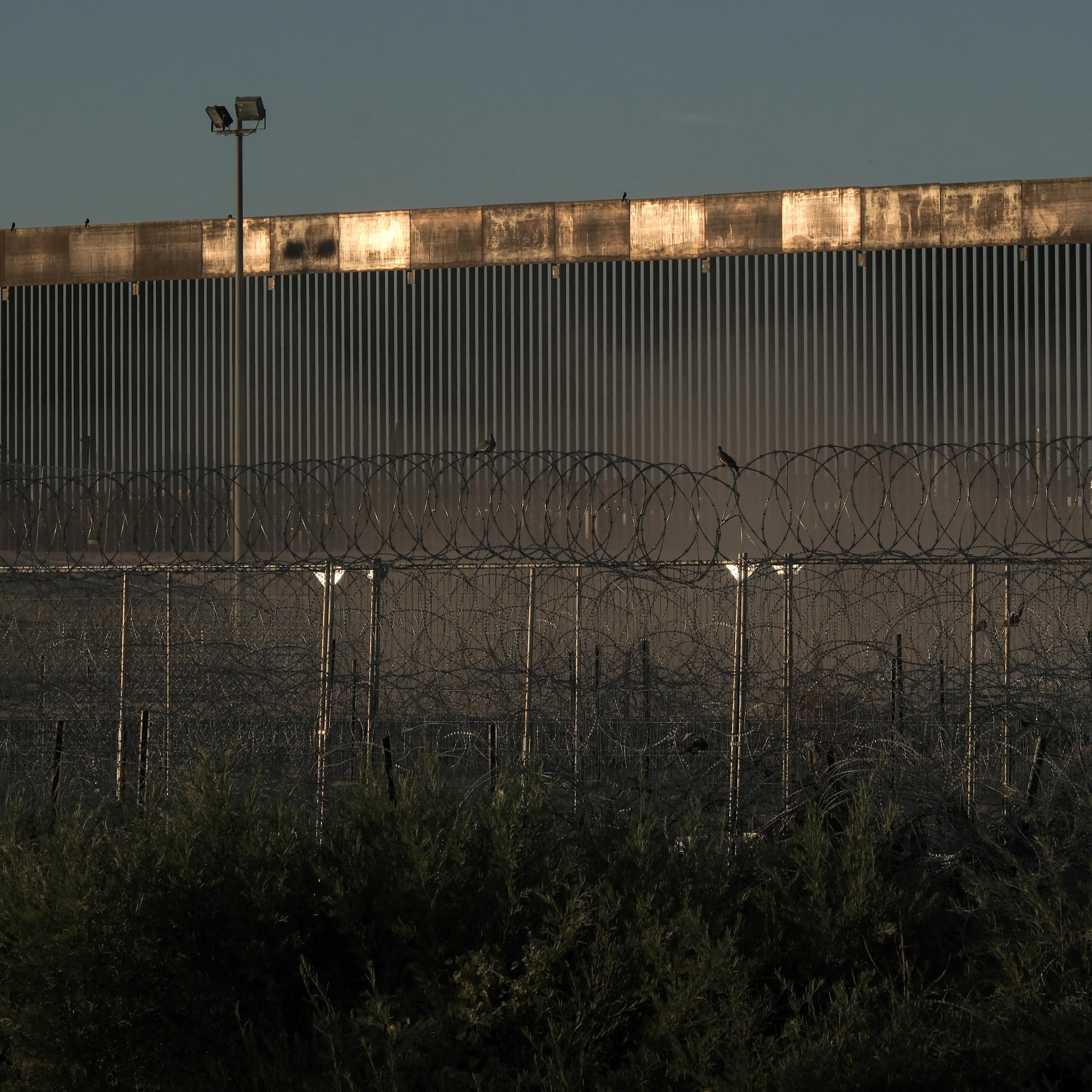 A large metal wall is seen in front of barbed wire.