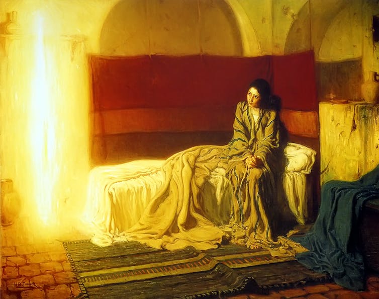 A young woman sitting on a bed, looking at a pillar of light.