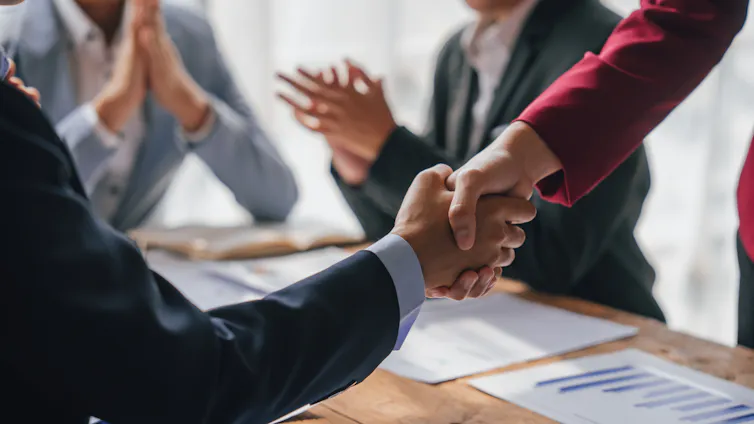 Close up of two people shaking hands while two other individuals clap in the background