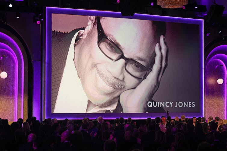 A photo of Quincy Jones on the big screen behind a large crowd in a hotel ballroom