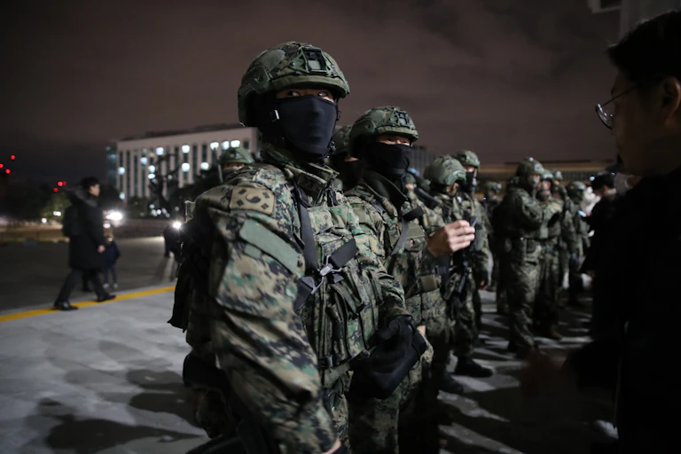 Fatigue-clad soldiers with masks covering their face stand outside a large building.