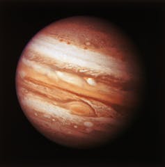 The planet Jupiter is encircled by light brown, dark brown and white bands.