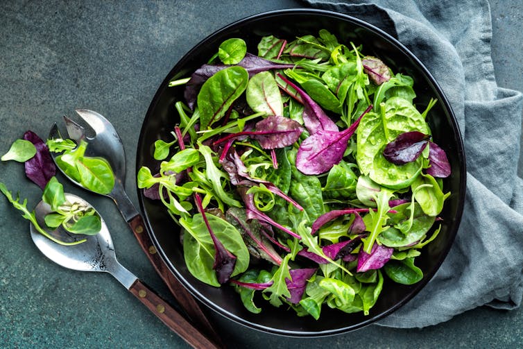 A leafy green salad in a bowl on the table with a serving spoon
