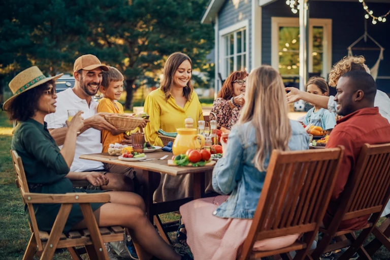 Family and friends around outside table eating and drinking in summer