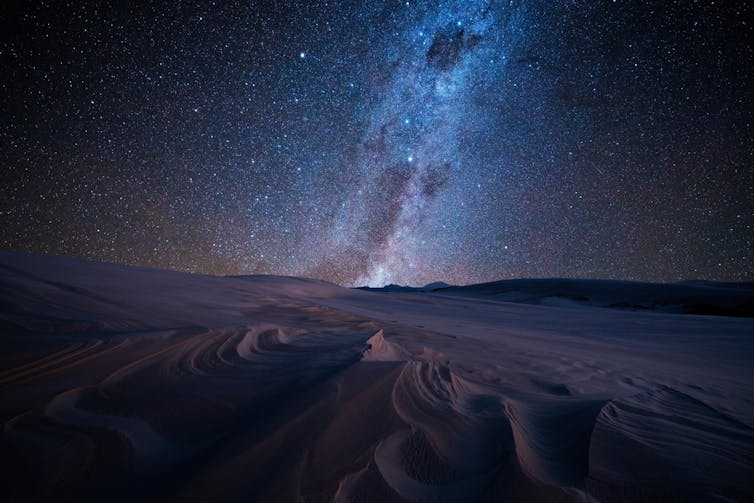 Bright stars shining above sand dunes.