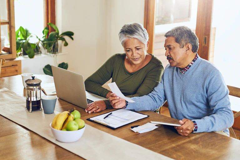 senior couple with bills, paperwork and receipt documents sat at a table